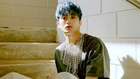 Mark Lee in a stylish outfit with unique accessories, captured in a sunlit stairwell.