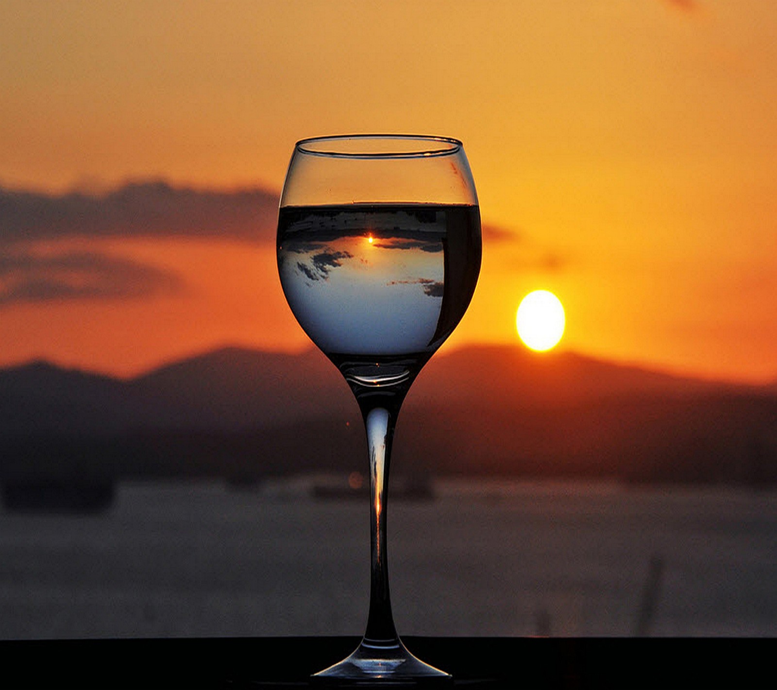 Ein glas wein auf einem tisch mit einem sonnenuntergang im hintergrund (schön, sonnenuntergang)