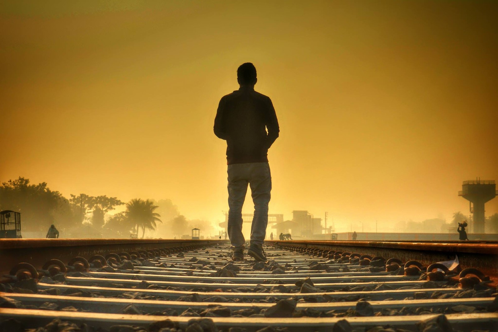 Homem árabe em pé nos trilhos do trem olhando o pôr do sol (ferrovia, trilha)