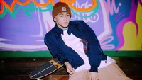 Mark Lee from NCT Dream in a casual urban setting, featuring vibrant graffiti and a skateboard.