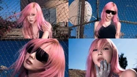 Un modèle aux cheveux roses portant des lunettes de soleil pose devant un décor urbain, dégageant une esthétique audacieuse et edgy.