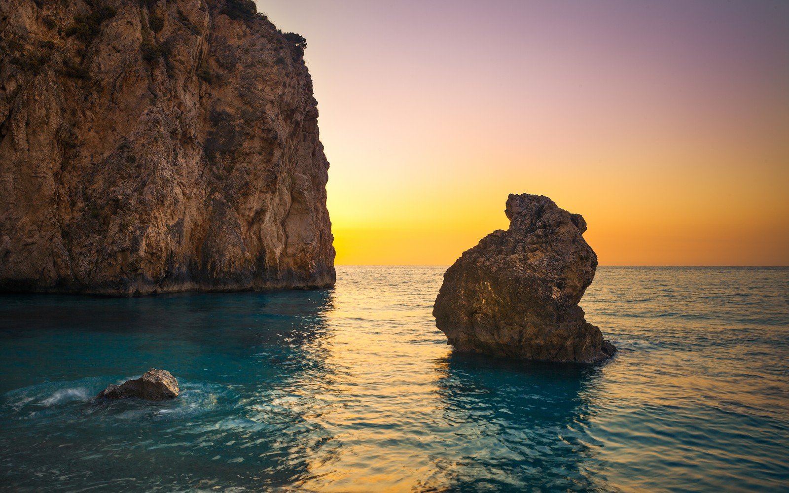 A view of the sun setting over the ocean and rocks (milos beach, greece, lefkada island, lone rock, sunset orange)