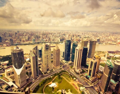 Luftaufnahme der lebhaften Skyline von Shanghai, die moderne Wolkenkratzer und eine pulsierende städtische Landschaft entlang des Flusses zeigt.