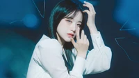 Shuhua de (G)I-DLE dans une pose captivante et artistique, mise en valeur par un fond bleu d'ambiance.