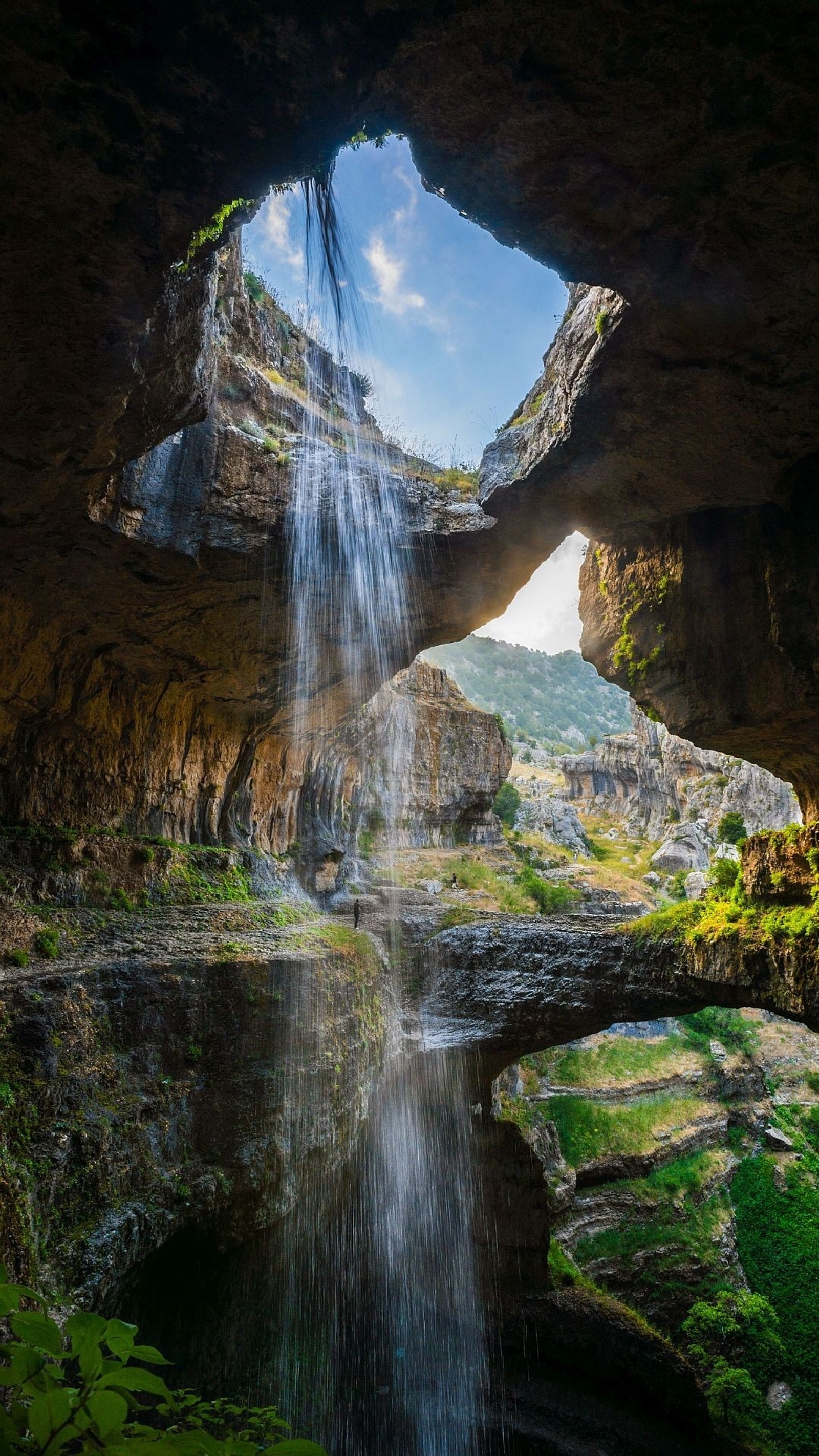 Vista de uma cachoeira saindo de uma caverna em um vale verde (viagem, natureza, água, nuvem, recursos hídricos)