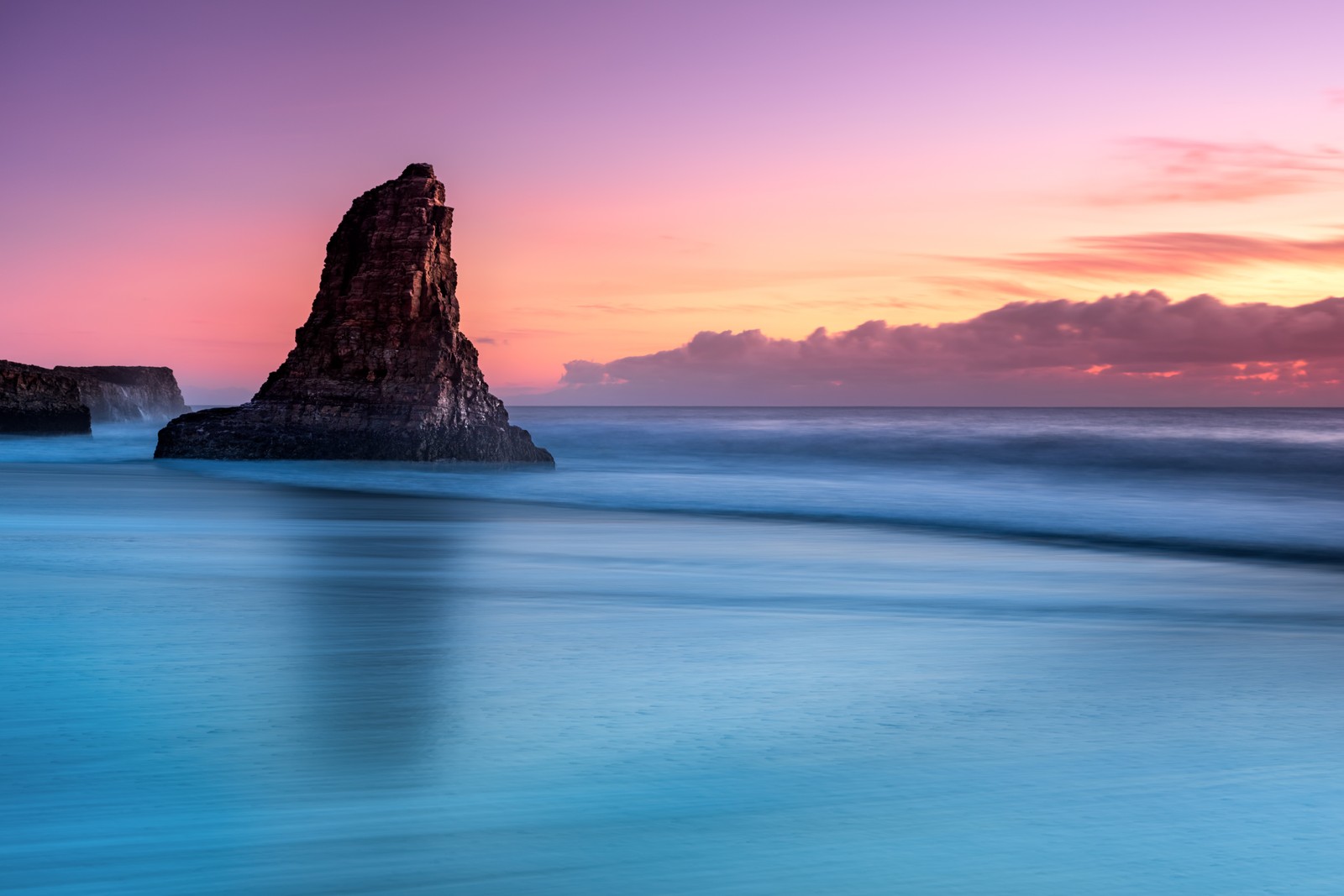 Una vista de una playa con una formación rocosa en el agua (agua, nube, atmósfera, recursos hídricos, paisaje natural)