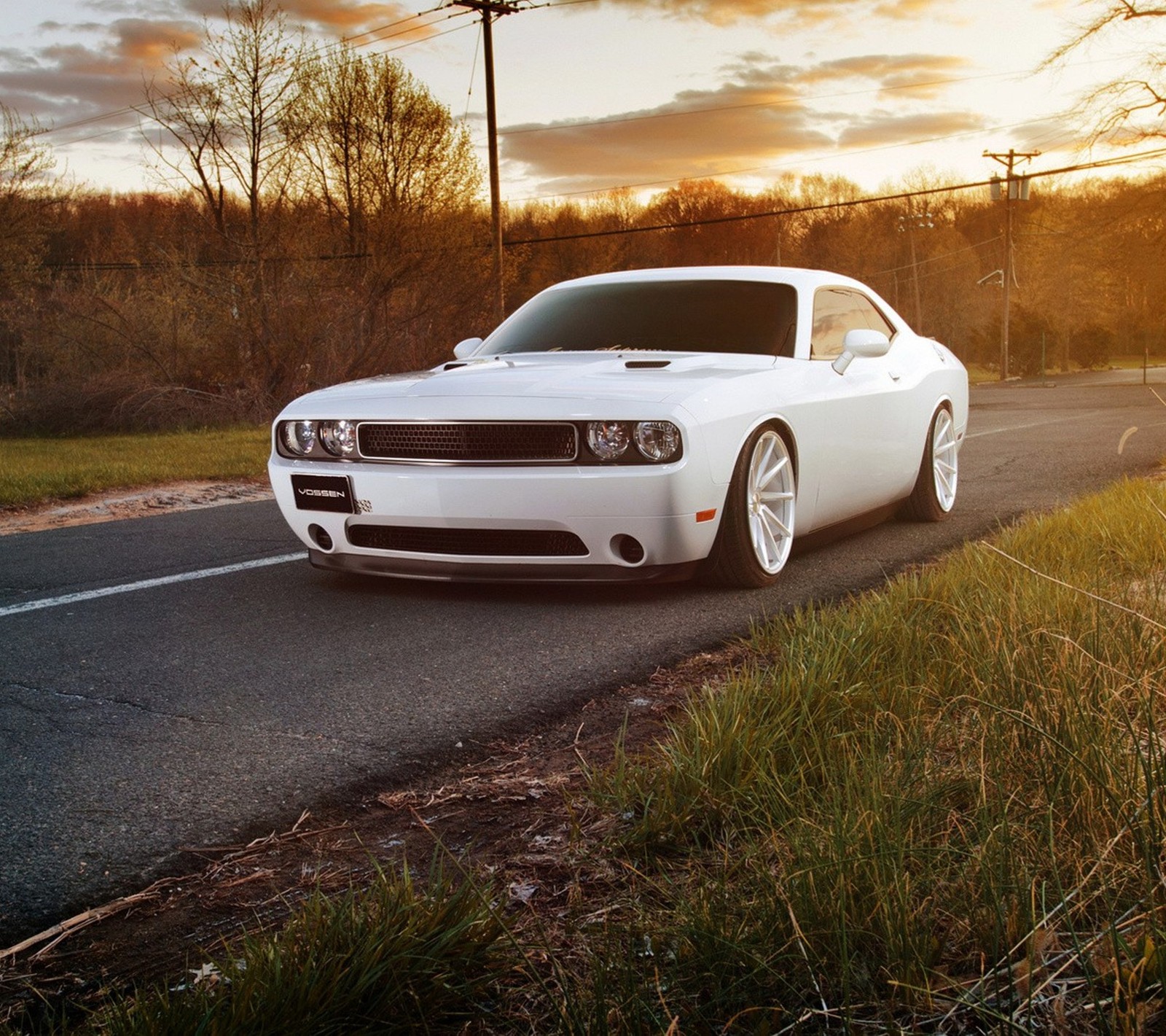 A close up of a white car parked on a road near a field (car, road, white)