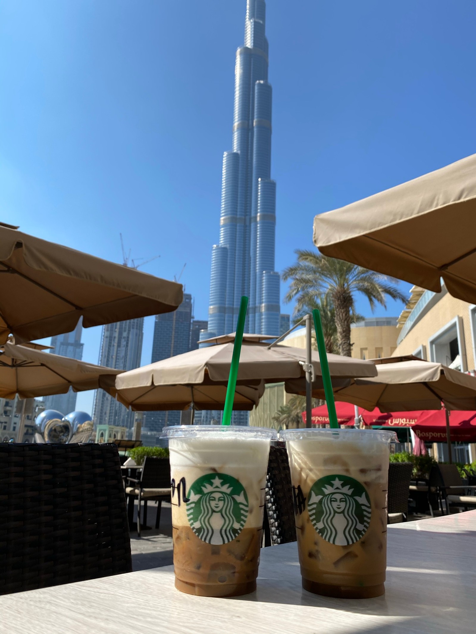 Starbucks iced coffee with a straw and a straw in front of a burjra tower (dubai, burj khalifa, tower, drink, fast food)