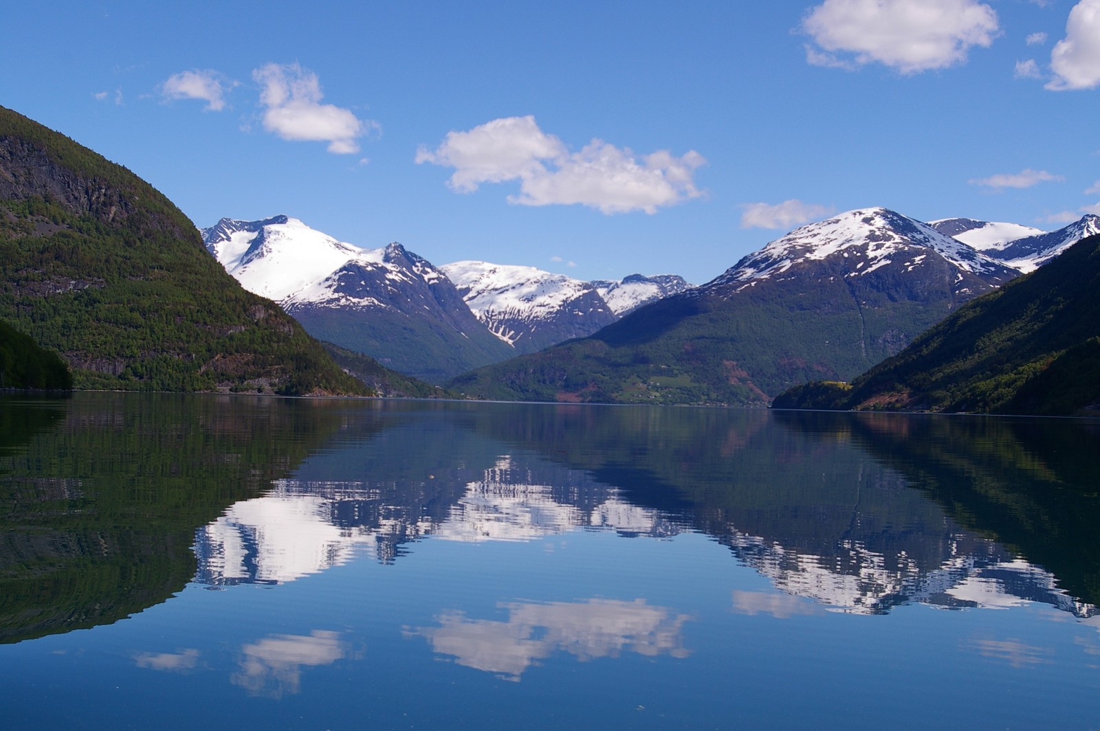 Montanhas refletidas em um lago com um barco em primeiro plano (natureza, fiorde, wild, montanha, reflexo)