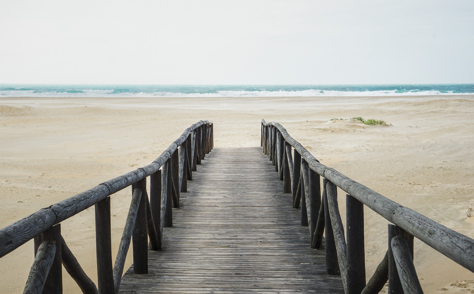 A close up of a wooden walkway leading to the beach (beach, shore, ocean, runway, water)