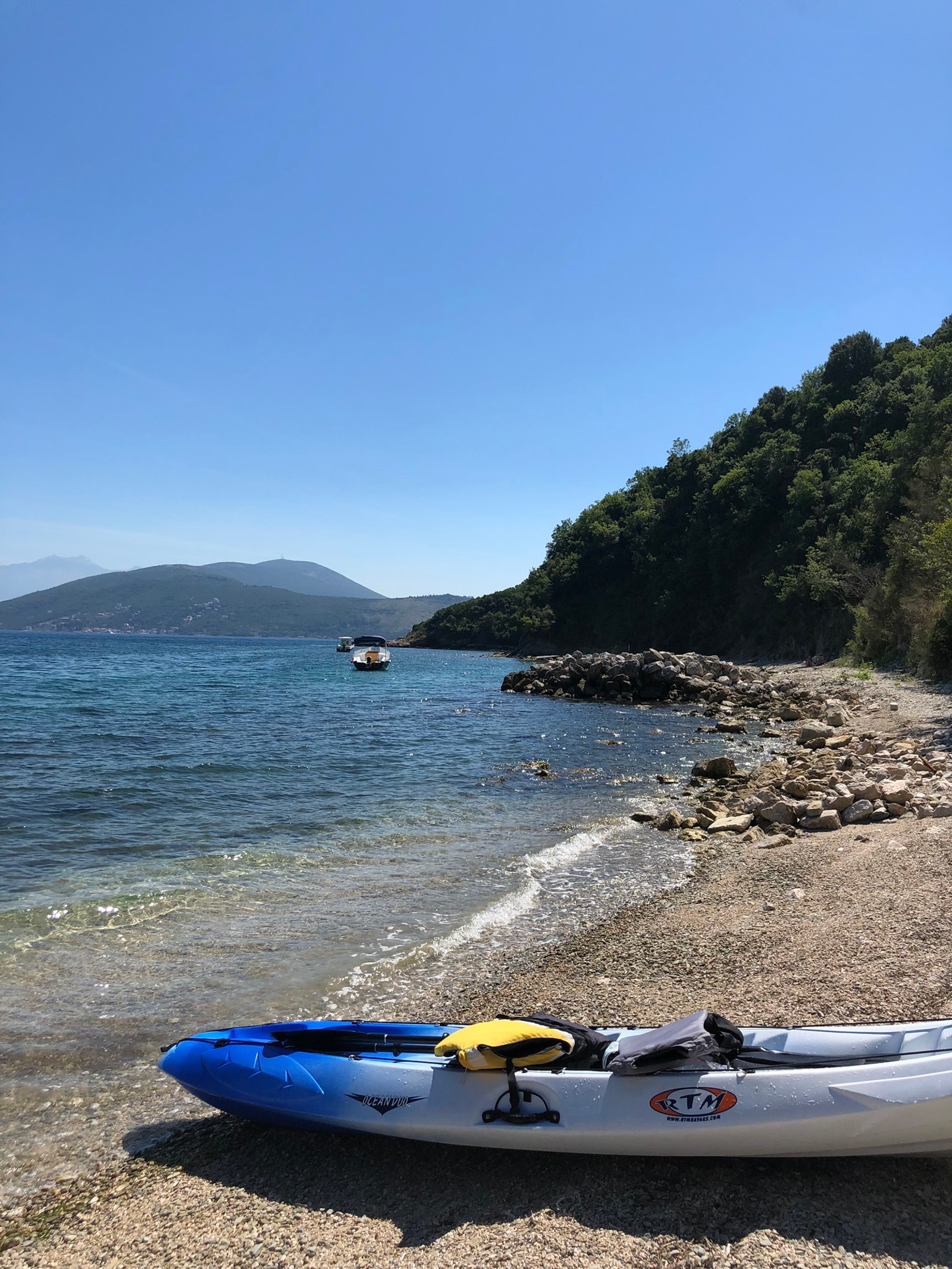 Há um caiaque na praia com um barco na água (mar, embarcação, costa, barco, colina)