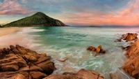 Serener australischer Strand bei Sonnenuntergang mit Küstenfelsen und sanften Wellen