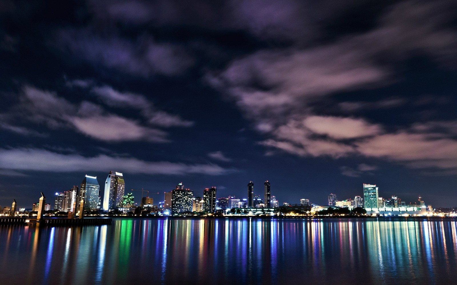 Vista da silhueta de uma cidade à noite com um lago em primeiro plano (apple macbook pro, maçã, paisagem urbana, cidade, linha do horizonte)