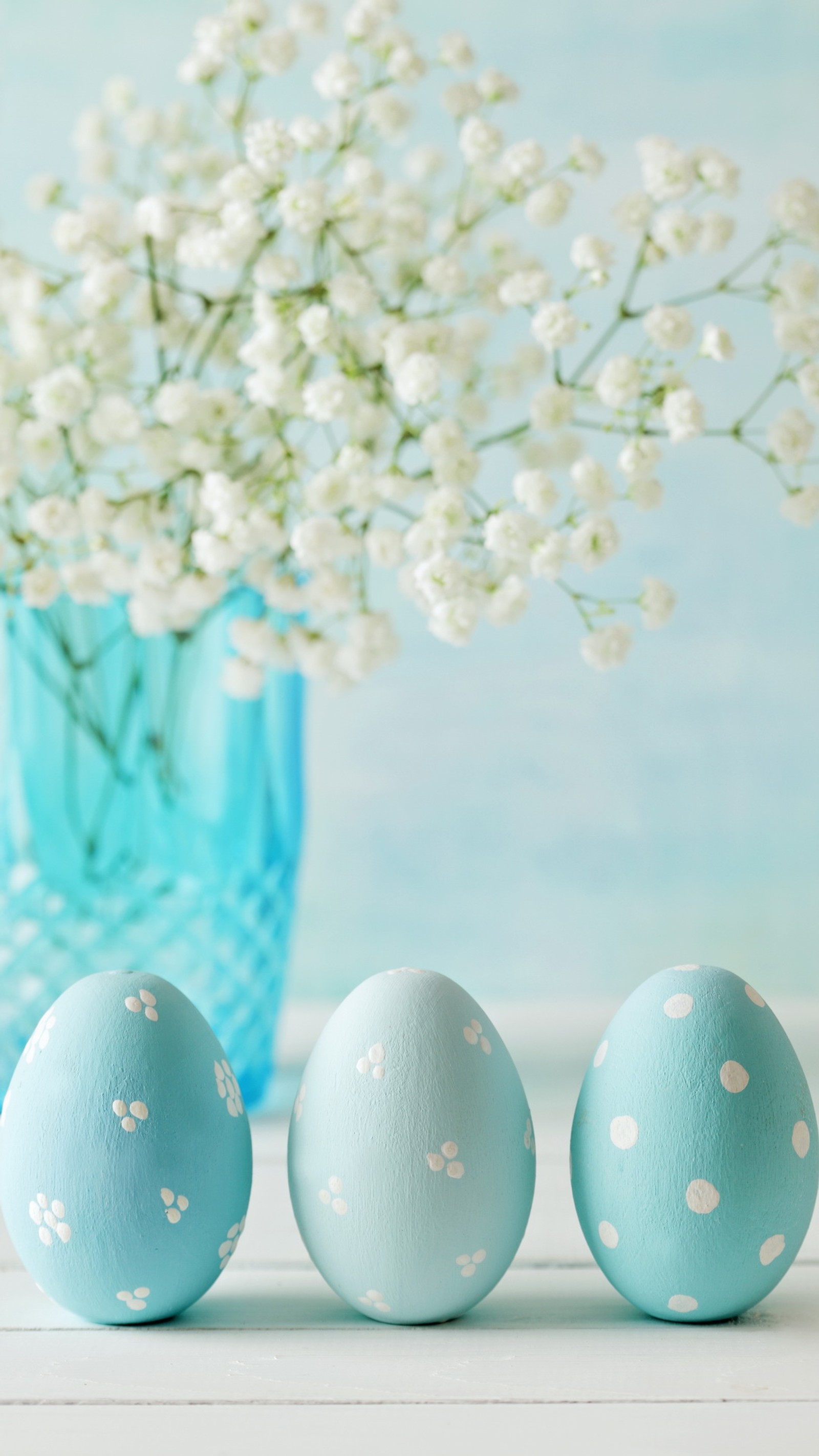 Trois œufs peints en bleu à côté d'un vase avec des fleurs blanches (bleu, décor, décoration, œuf, fleurs)