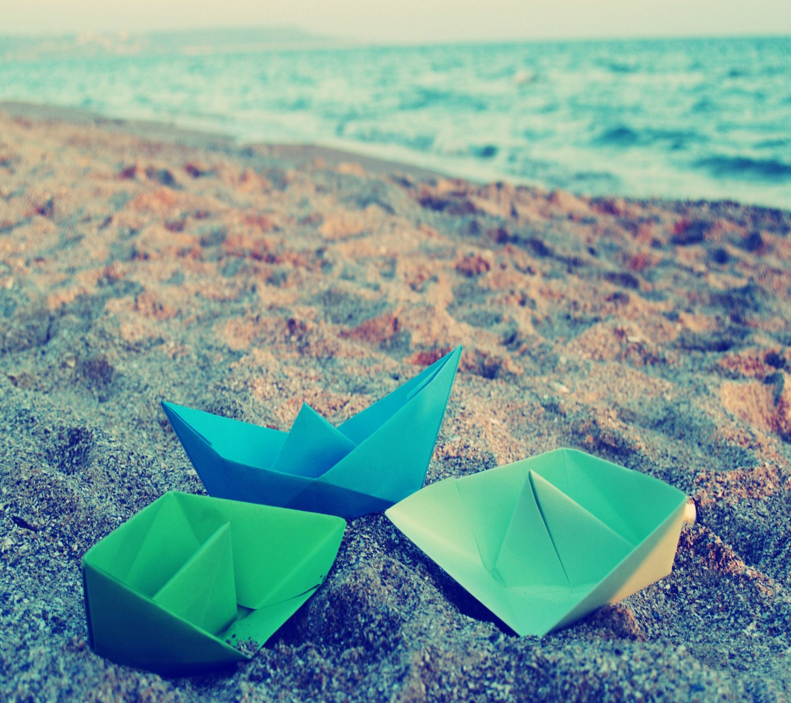 Três barcos de papel estão na areia perto do oceano (praia, barcos de papel)