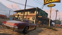 Un coche clásico estacionado fuera de una tienda de comestibles rústica en el mundo abierto de Grand Theft Auto V.