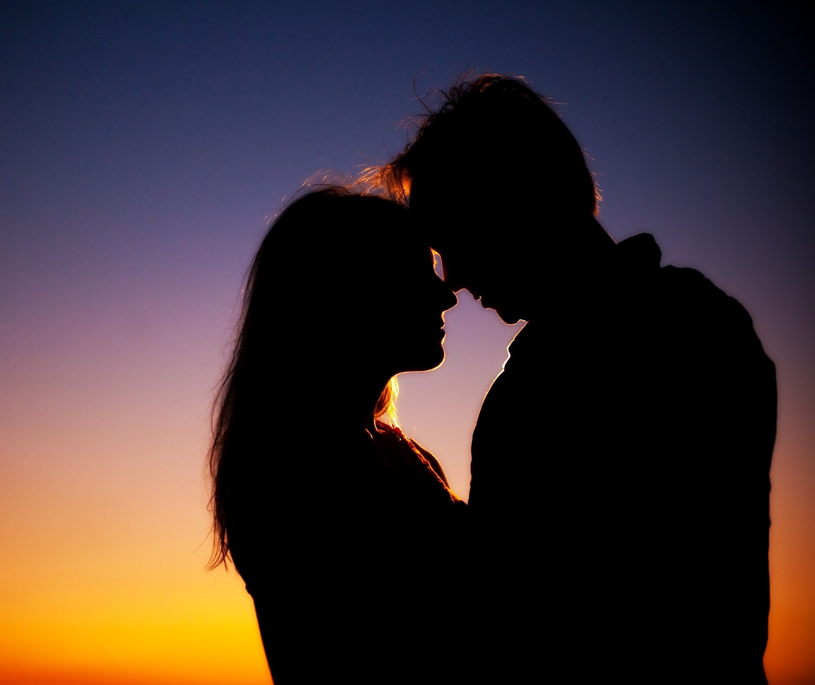 Silhouette of a couple kissing at sunset with the sun setting in the background (meem, rubab)