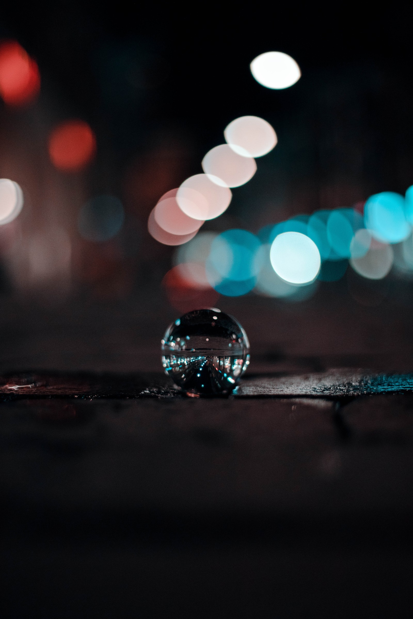 A close up of a glass ball on a sidewalk at night (bokeh, depth of field, reflection, water, light)