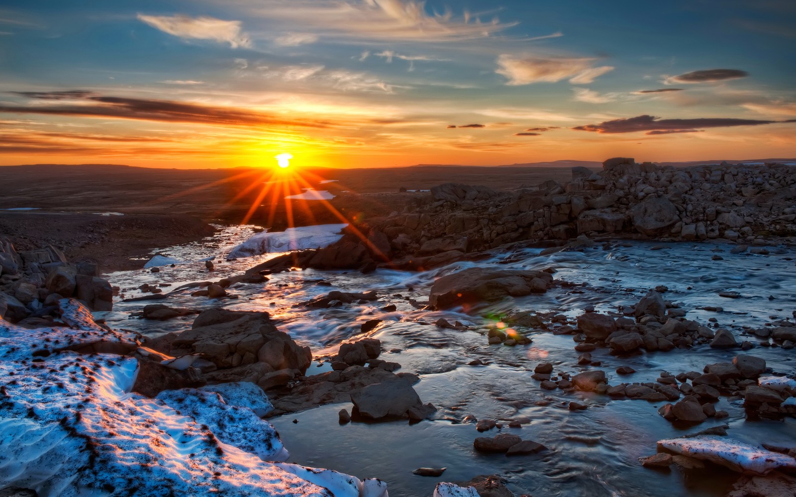 A sunset over a river with snow and rocks in the foreground (sunrise, rock, mountain, desert, terrain)