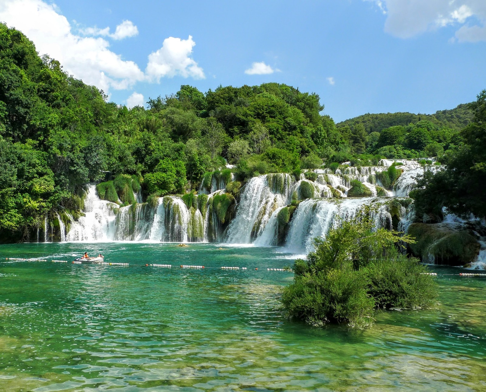 A view of a waterfall with people in a boat in the water (croatia, krka, summer, waterfall)