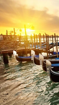 Gondolas at sunset along the Grand Canal, reflecting golden sunlight.