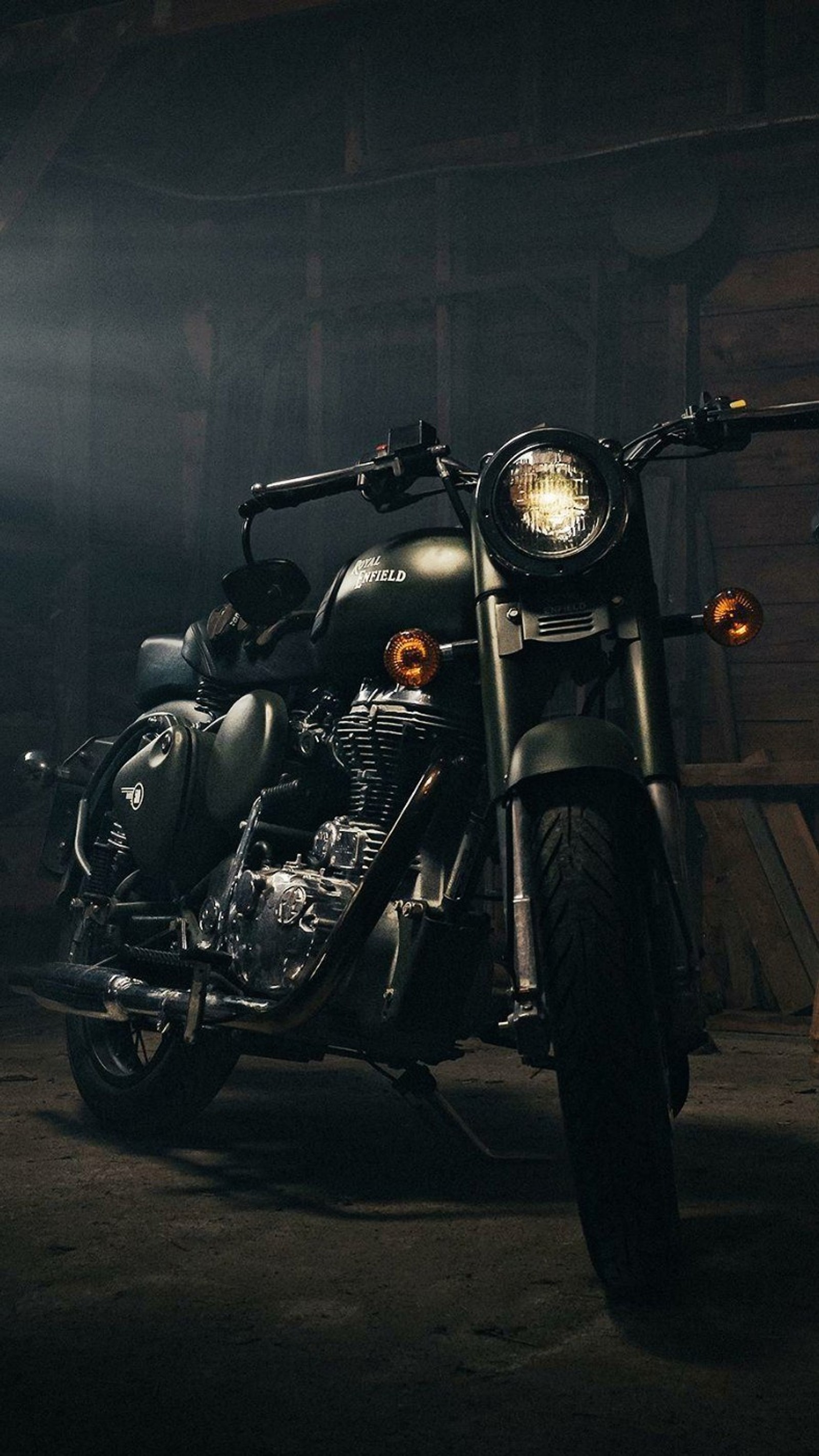 There is a motorcycle parked in a garage with a light on (bullet, classic, enfield, royal)