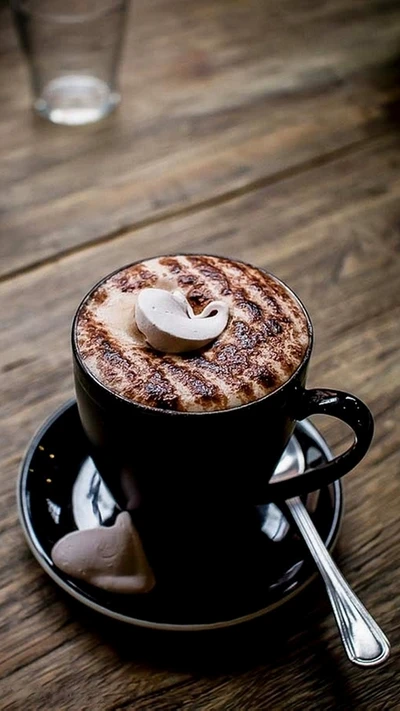 Cappuccino rico coberto com cacau, servido em uma xícara preta com um delicado suspiro ao lado.