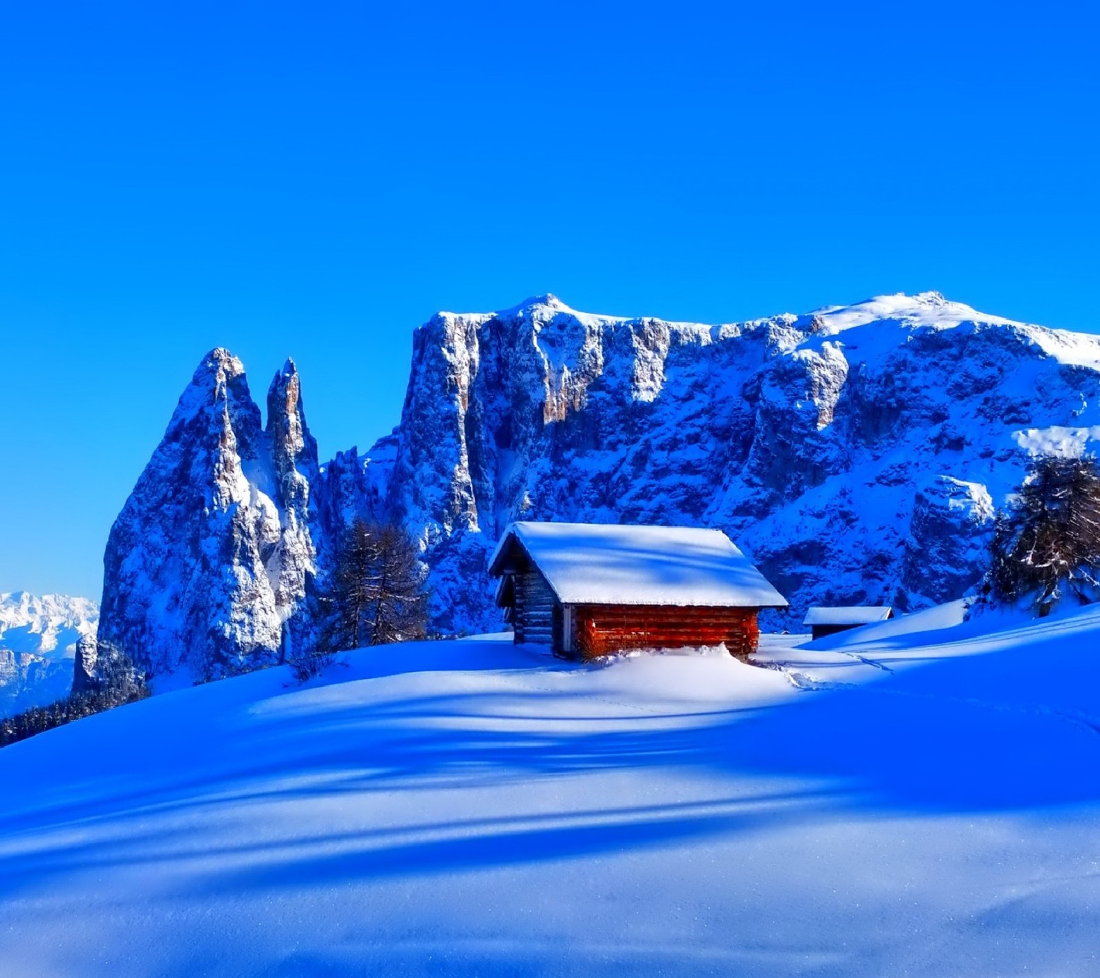 Snowy mountain scene with a cabin in the foreground and a blue sky (winter)