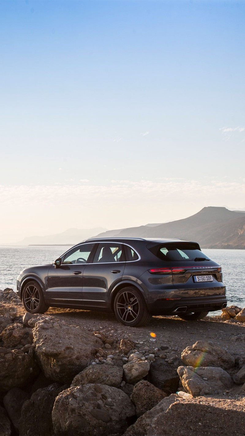 Un primer plano de un coche estacionado sobre rocas cerca del agua (2017, 2018, playa, coches, cayena)