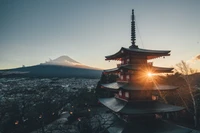 Sunset over Mount Fuji, framed by a traditional pagoda and winter trees, with a serene view of Lake Kawaguchi.