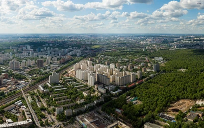 Ein Panoramablick auf die städtische Landschaft Moskaus, der dichte Grünflächen mit weitläufigen Stadtstrukturen unter einem lebhaften Himmel verbindet.