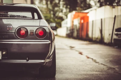 Nissan Skyline GT-R garé dans une ruelle urbaine, mettant en valeur son design arrière emblématique et son éclairage automobile.