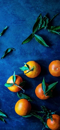 Clementines and Green Leaves on a Blue Surface