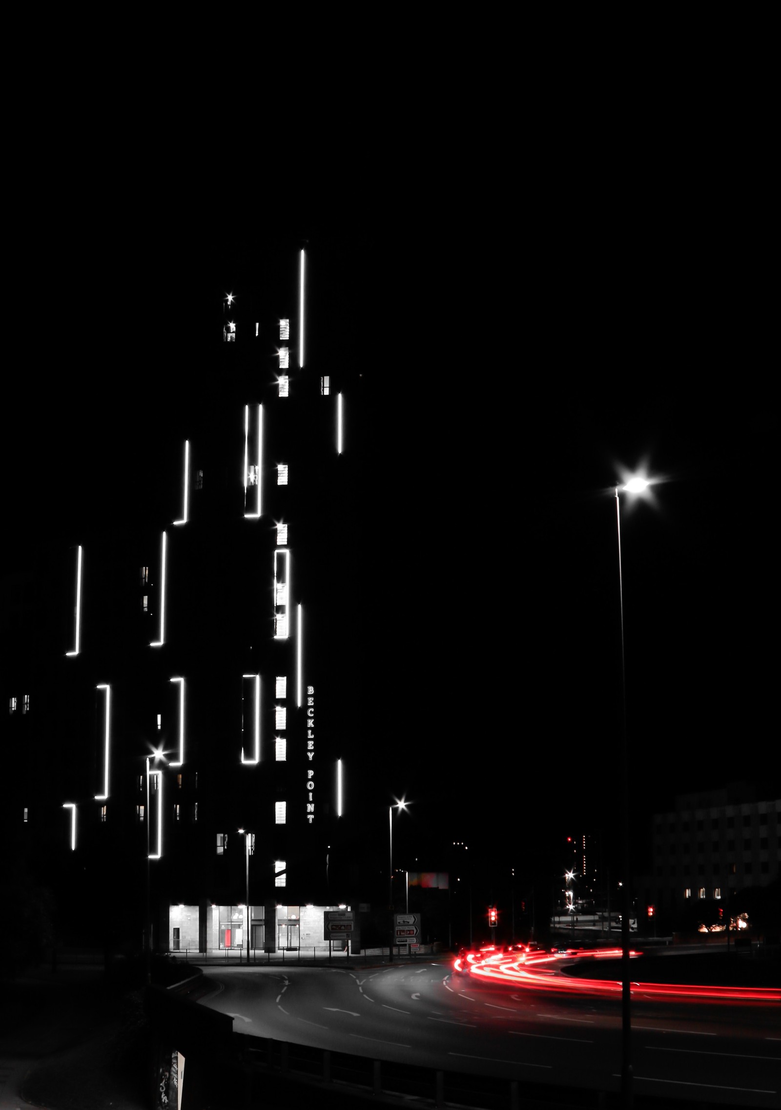 Foto noturna de uma rua da cidade com um prédio iluminado à noite (preto, escuridão, branco, noite, poste de luz)