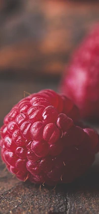 Gros plan d'une framboise rouge vibrante, mettant en valeur sa surface texturée et sa beauté naturelle sur un fond rustique.