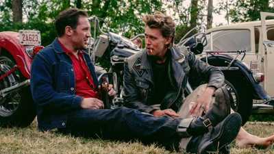 A candid moment between two biker characters, surrounded by vintage motorcycles.