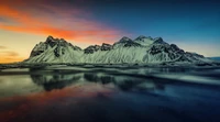 Montanhas Vestrahorn ao pôr do sol, refletindo em um lago tranquilo, exibindo uma paisagem deslumbrante de picos cobertos de neve e céus vibrantes.