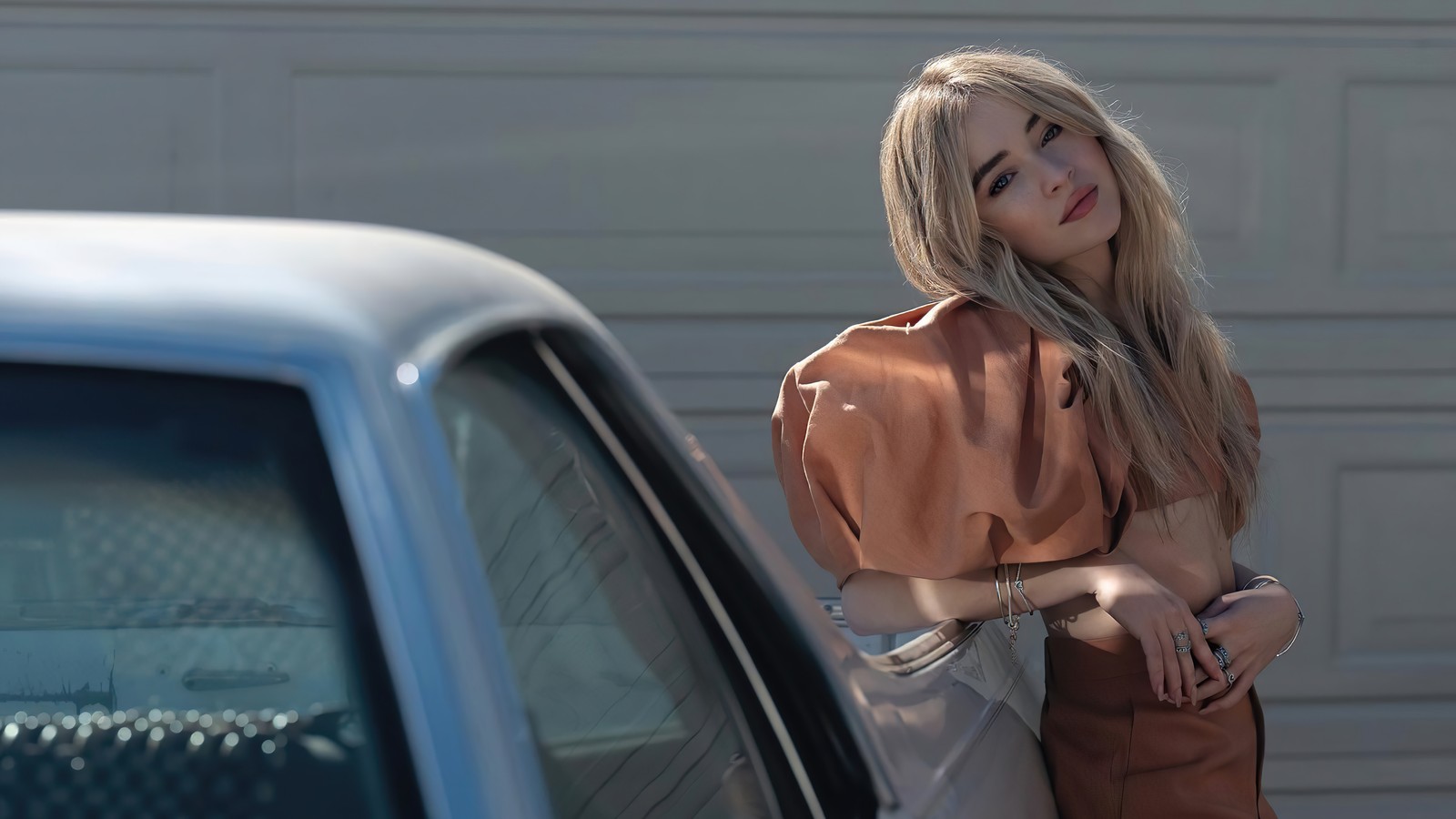 Mujer rubia apoyada en un auto frente a una puerta de garage (sabrina carpenter, estadounidense, cantante, celebridad, mujeres)