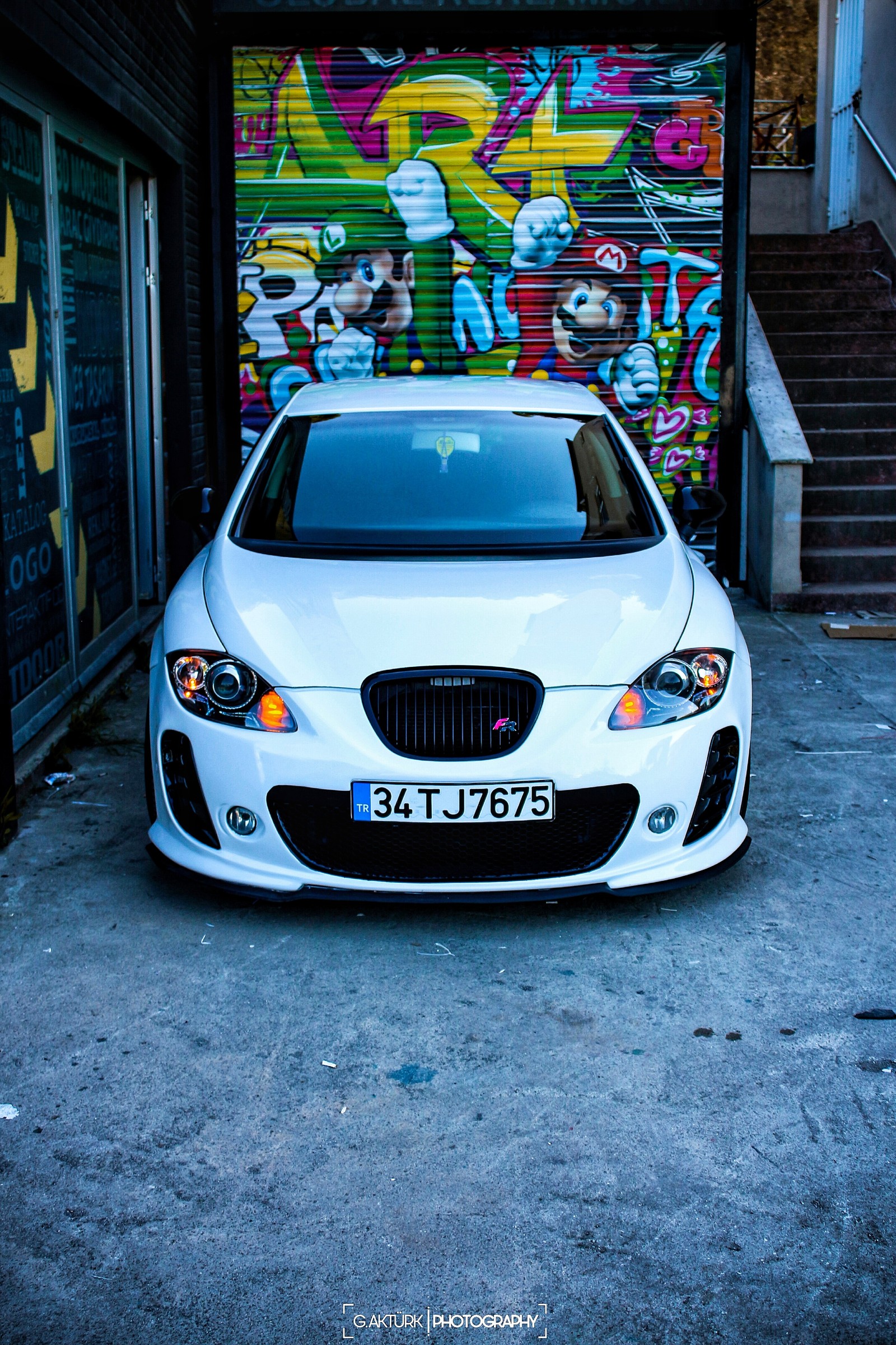 Une voiture blanche garée devant un garage avec des graffitis sur le mur (voiture, voitures, fr, léon, leon)