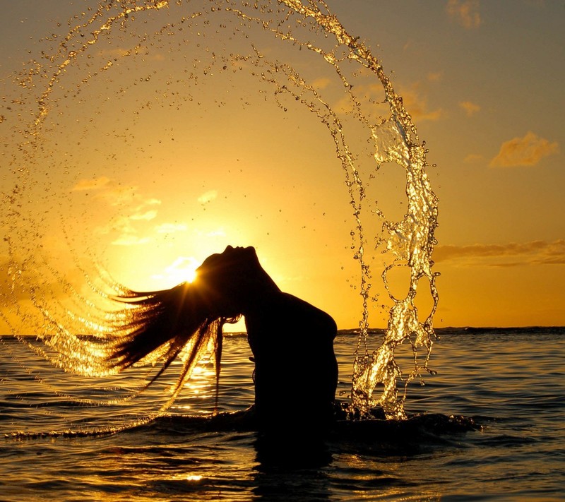 Eine arabische frau, die bei sonnenuntergang wasser im ozean spritzt (wasser, woda)