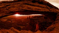 Sonnenaufgang über dem ikonischen Naturbogen im Arches Nationalpark, eingerahmt von rauen roten Felsformationen und weitläufigen Wüstenlandschaften.