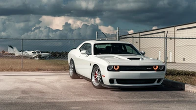 Мускул-кар Dodge Challenger припаркован рядом с ангаром для самолетов