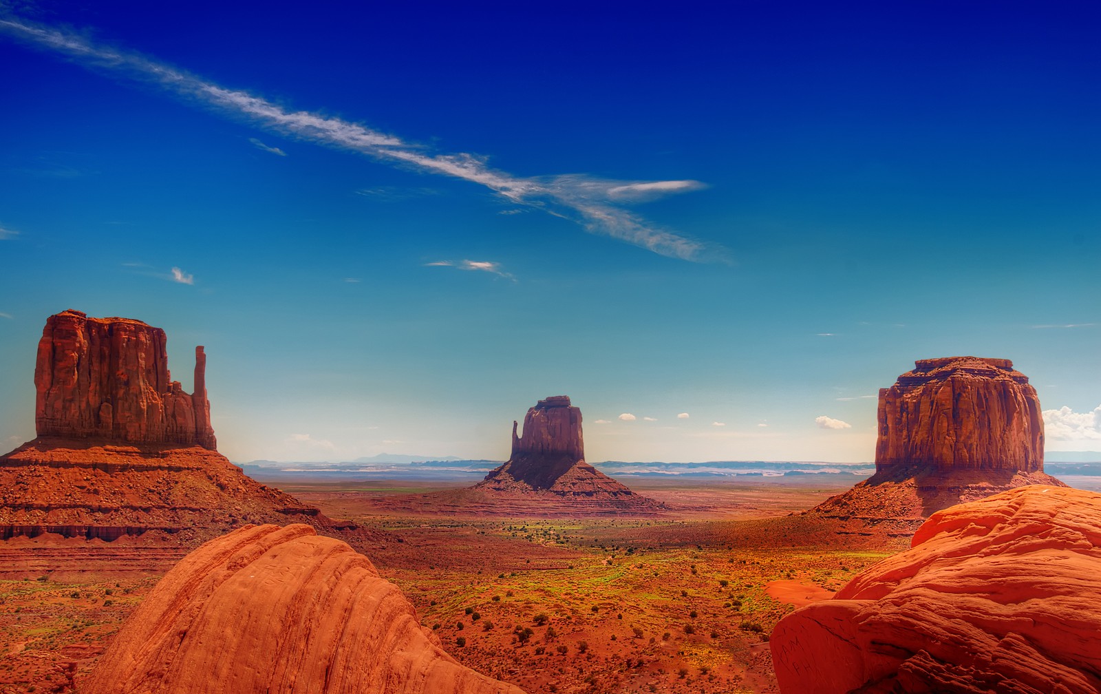 Une vue du désert avec quelques rochers au premier plan (monument valley, vallée, butte, formation, roche)