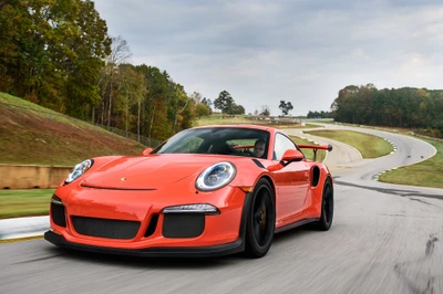 Porsche 911 GT3 en orange vif, courant sur une piste entourée de feuillage d'automne.