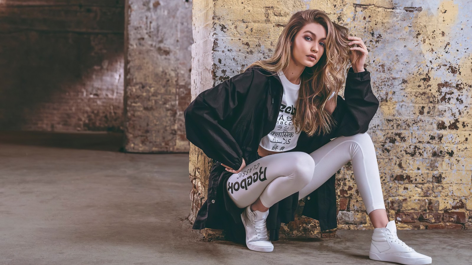 Una mujer sentada en un piso de concreto con una chaqueta negra y leggings blancos (gigi hadid, reebok, sesión de fotos, modelo, celebridad)