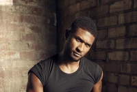 Portrait of a male artist exuding cool confidence, showcasing a stylish hairstyle against a textured brick wall.