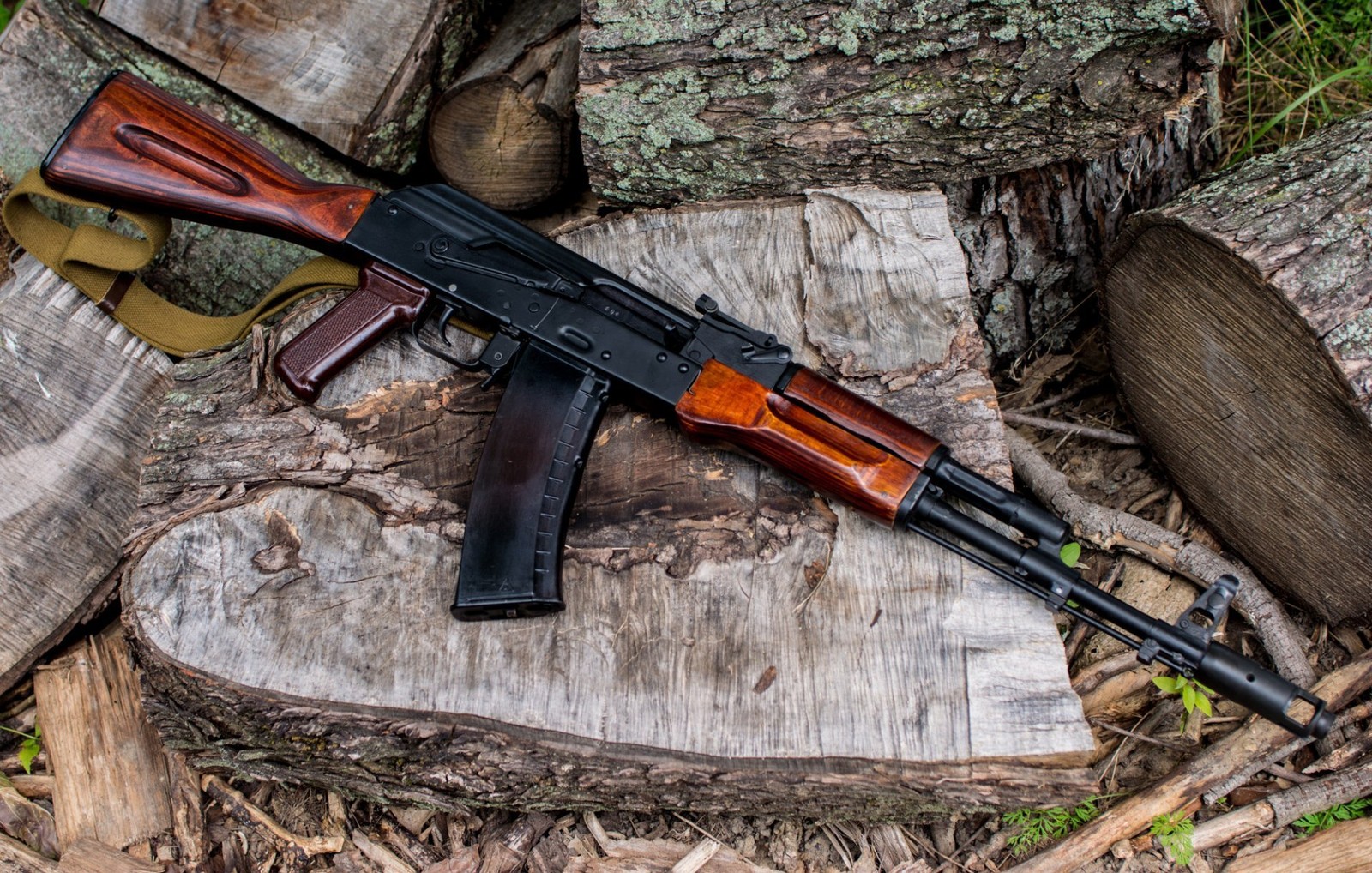 Rifle on a log with a sling attached to it (ak 74, firearm, gun, rifle, trigger)