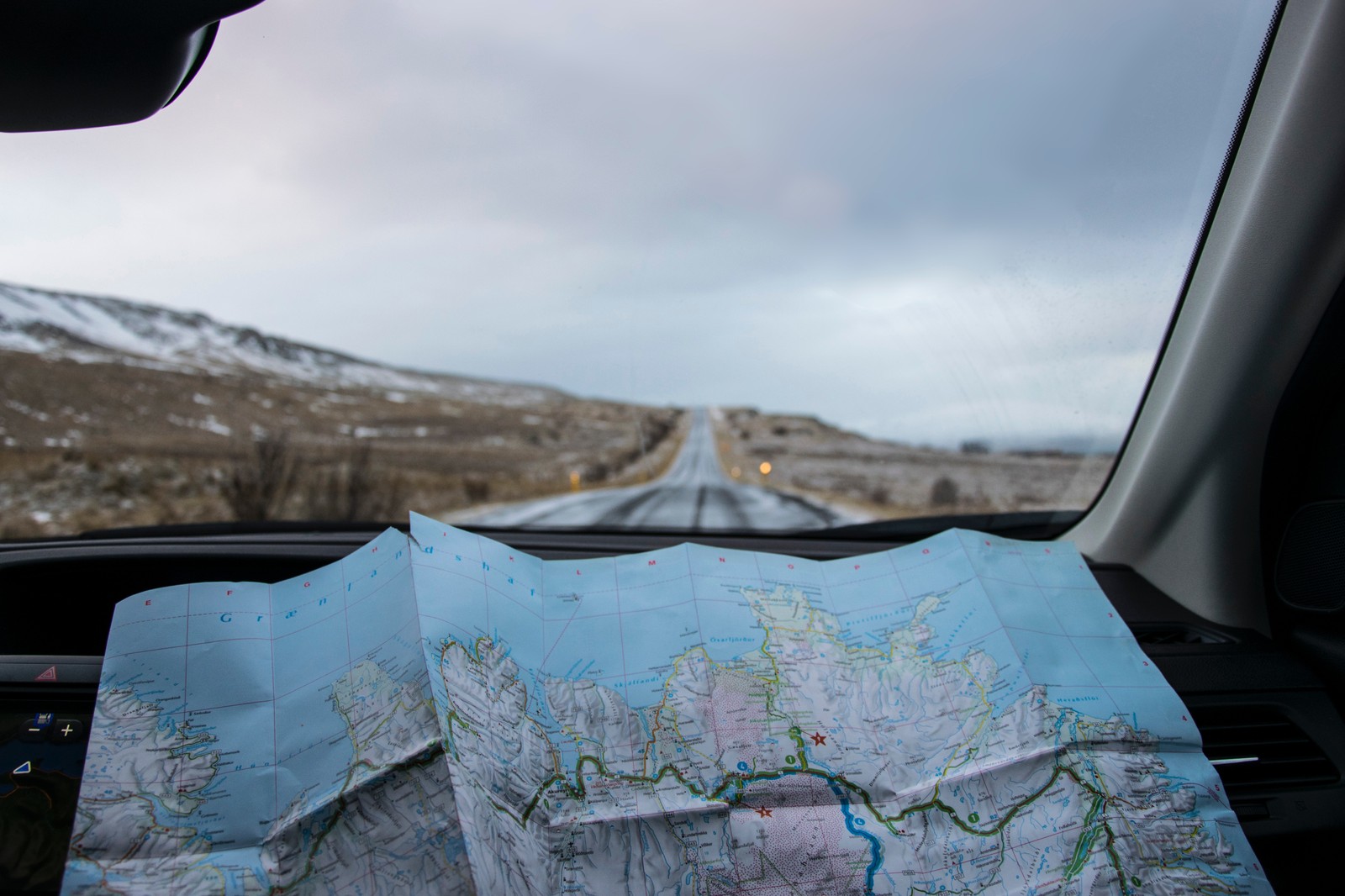 Um mapa no painel de um carro com vista para uma estrada (viagem, viagem de carro, férias, para brisa, vidro)