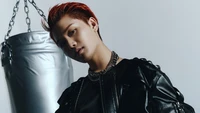 Taeil de NCT 127 présente un look frappant dans une tenue en cuir contre un fond minimaliste, dégageant une ambiance audacieuse et féroce.