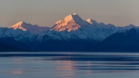 Majestoso amanhecer sobre o Lago Pukaki, refletindo os picos cobertos de neve da cordilheira da Nova Zelândia contra um céu matutino sereno.